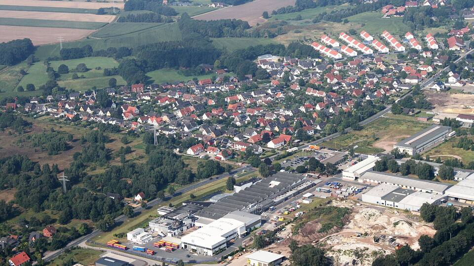 An aerial view of a residential area with houses, a large industrial complex, and surrounding fields.