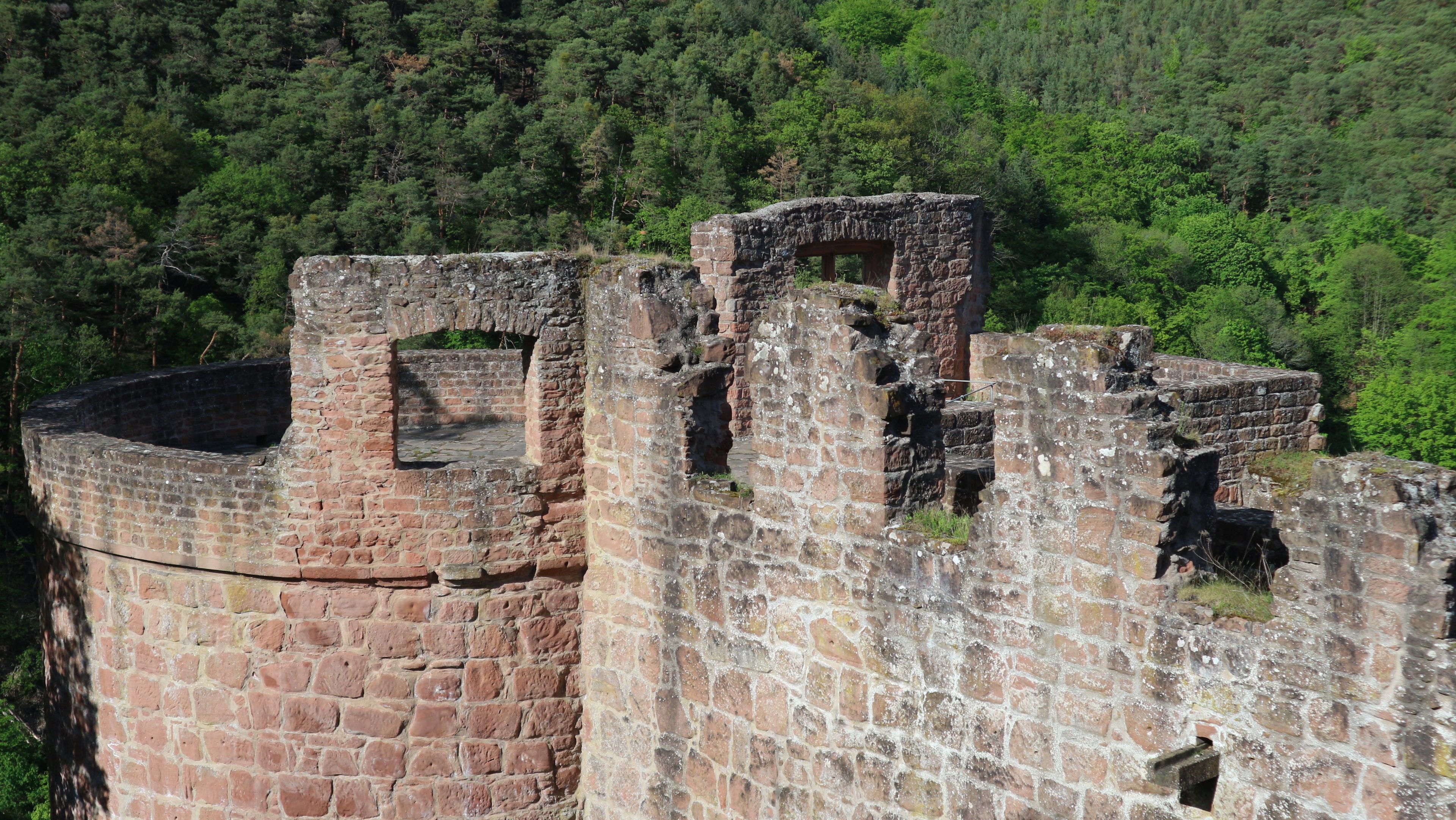 A historic stone fortification with multiple towers and walls, surrounded by dense forest.