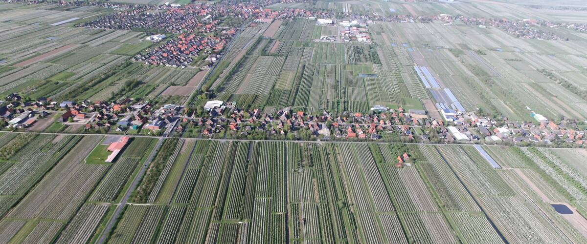 An aerial view of a rural area with organized agricultural fields, a small village, and a large water body.