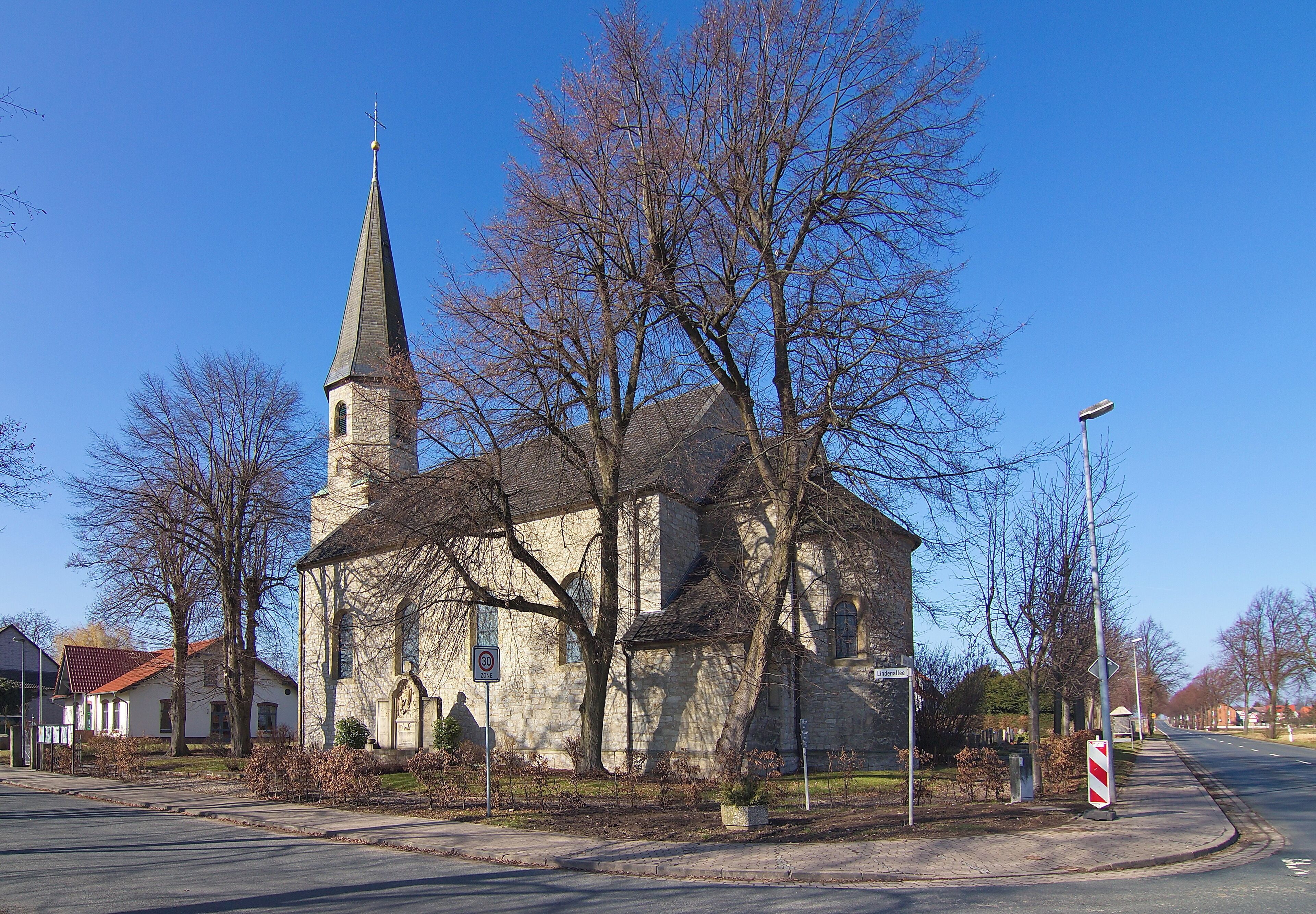 A church with a tall steeple and a red roof, surrounded by leafless trees and a clear blue sky.