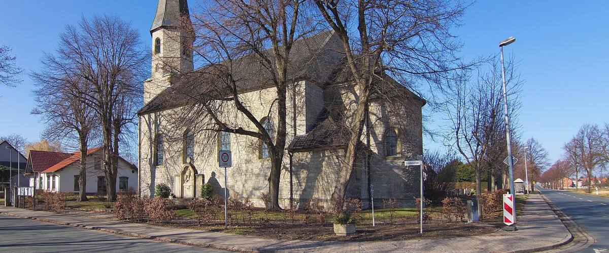 A church with a tall steeple and a red roof, surrounded by leafless trees and a clear blue sky.