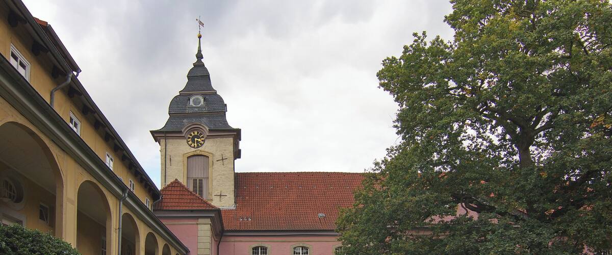 A historic building with a clock tower, arched walkways, and a well-maintained lawn.