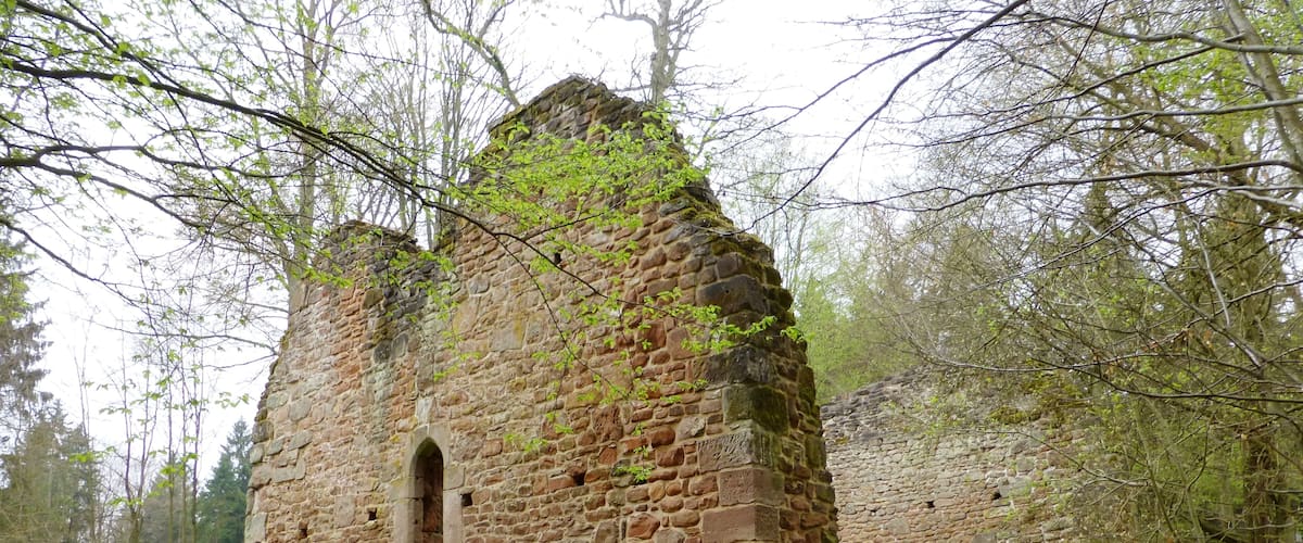 A stone ruin with a small arched window, surrounded by trees and grass.