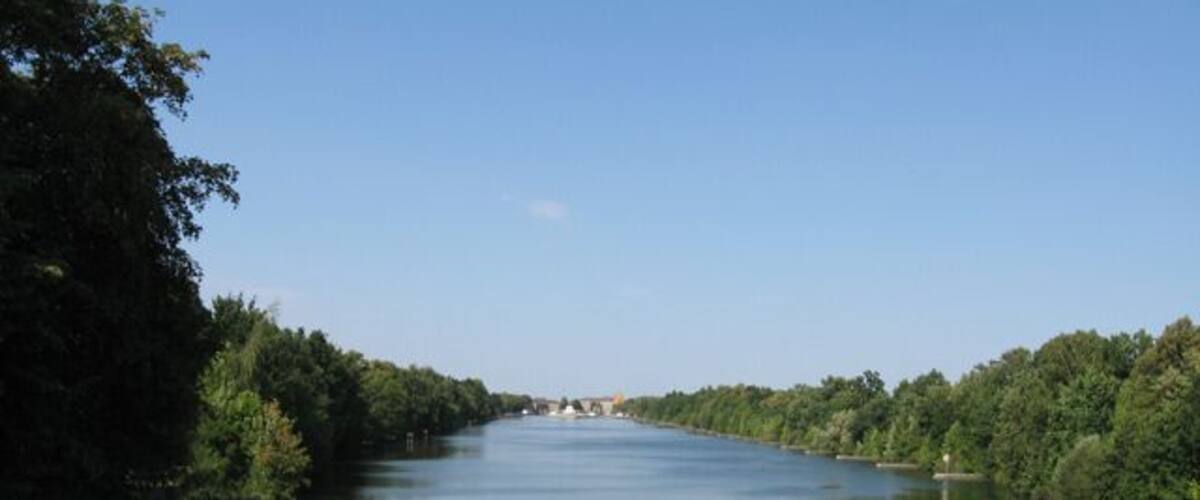 A calm river flanked by dense trees under a clear sky.