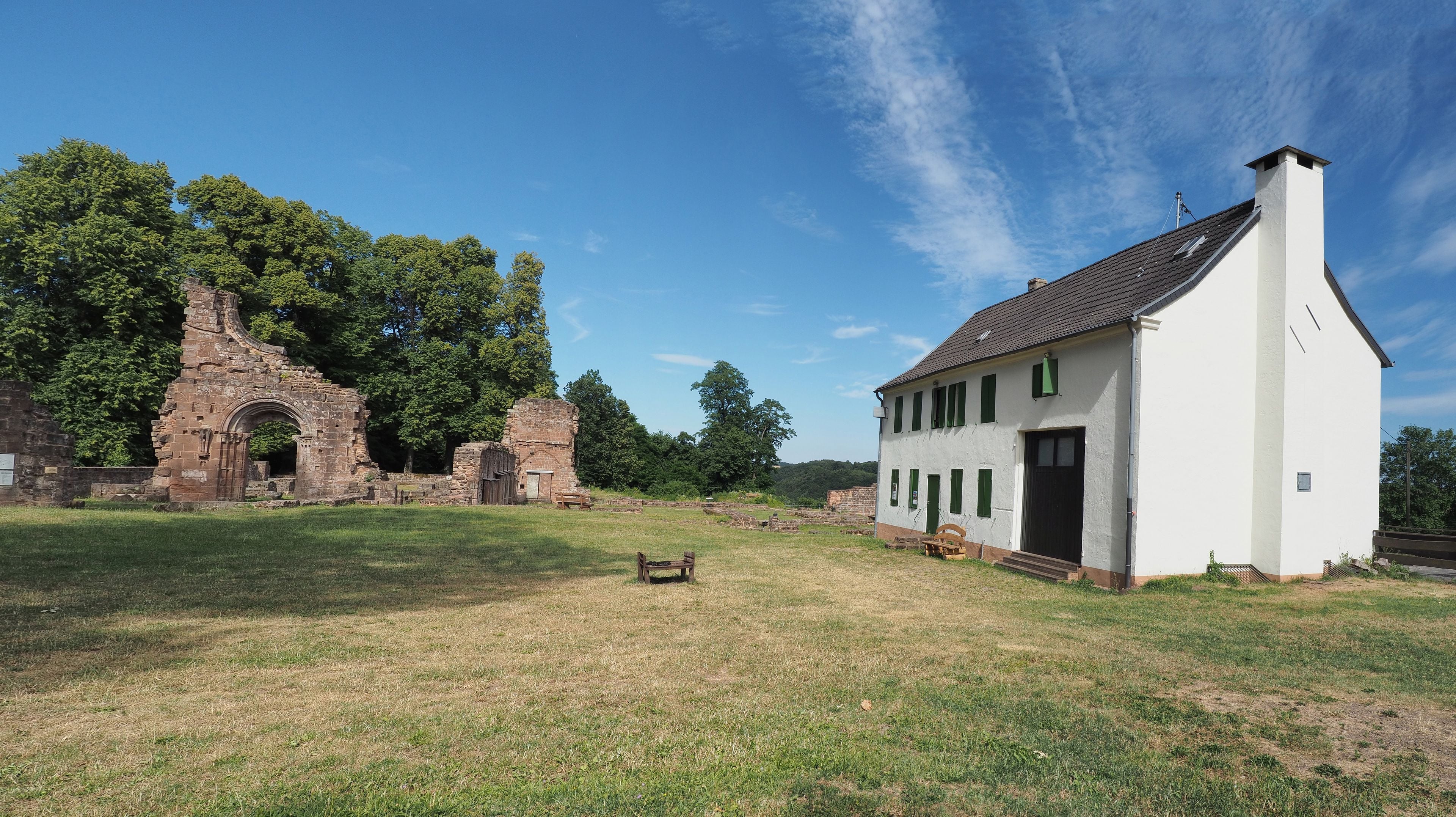 A historical site with ruins and a white building with green shutters.