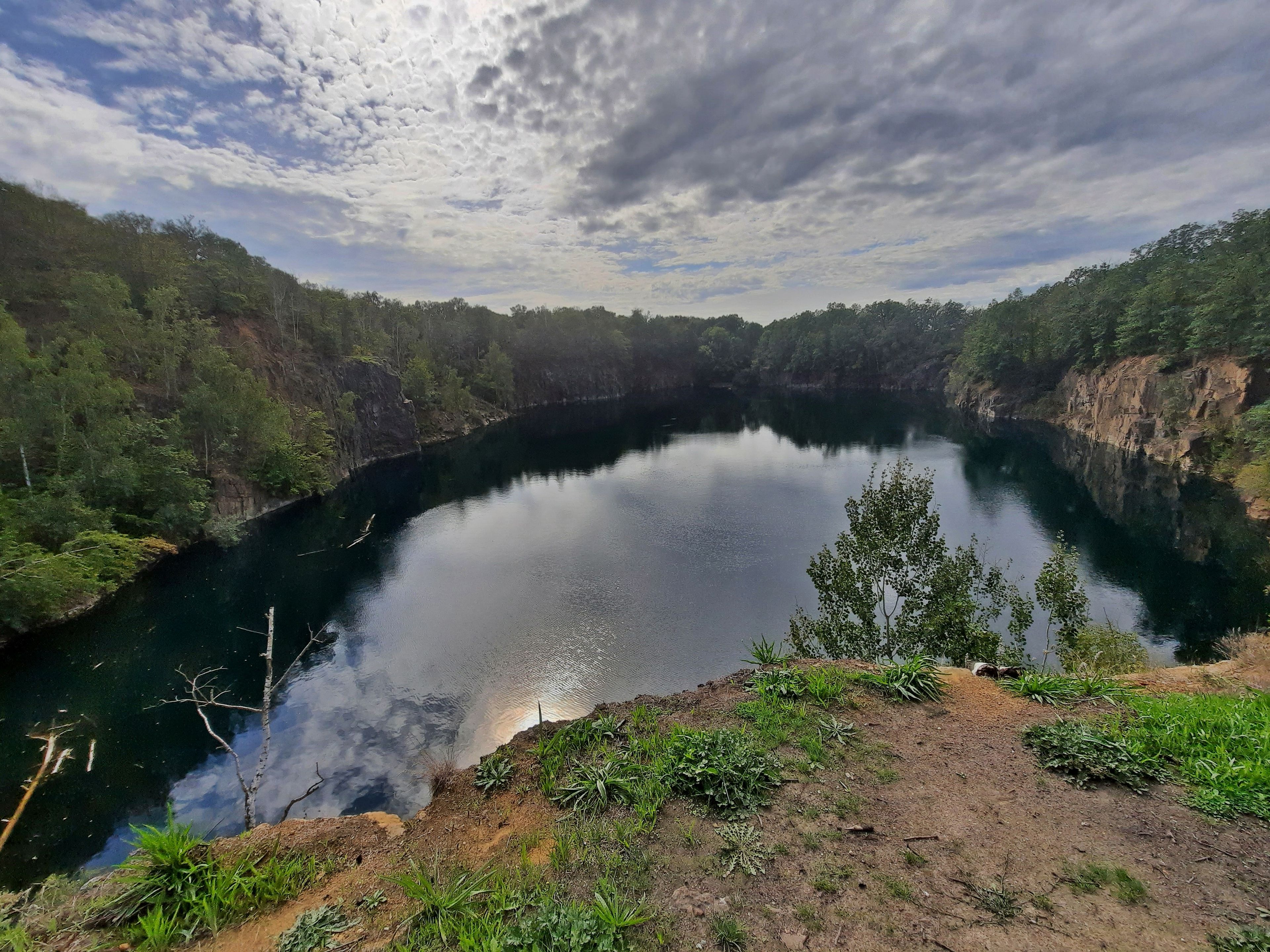 A serene lake surrounded by dense forest and rocky cliffs under a cloudy sky.
