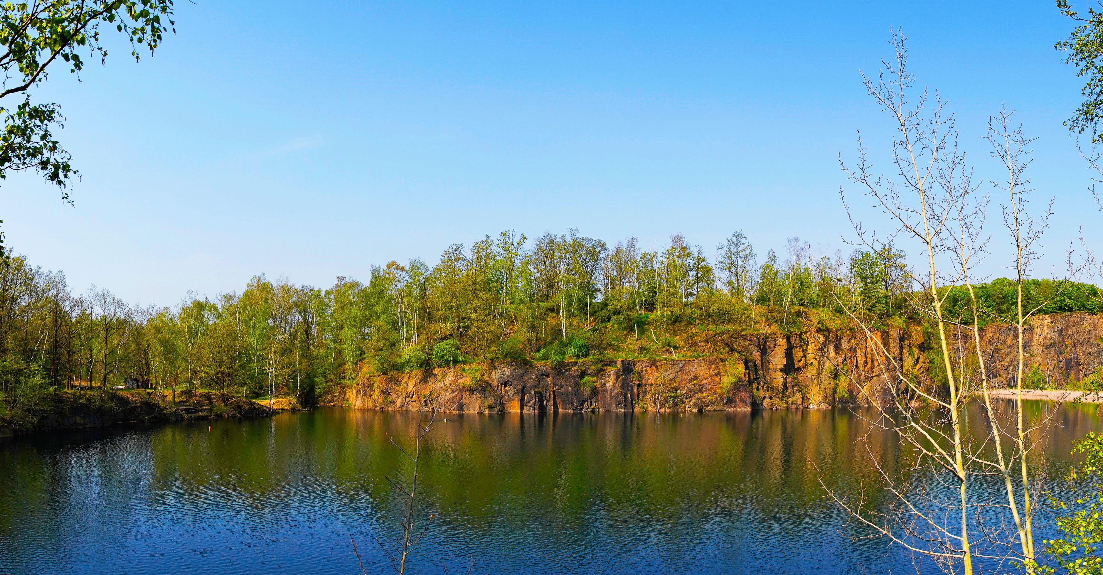 Un lago tranquilo rodeado de árboles densos y acantilados rocosos.