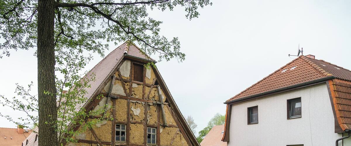 A traditional half-timbered house with a steep roof, adjacent to a modern white house.