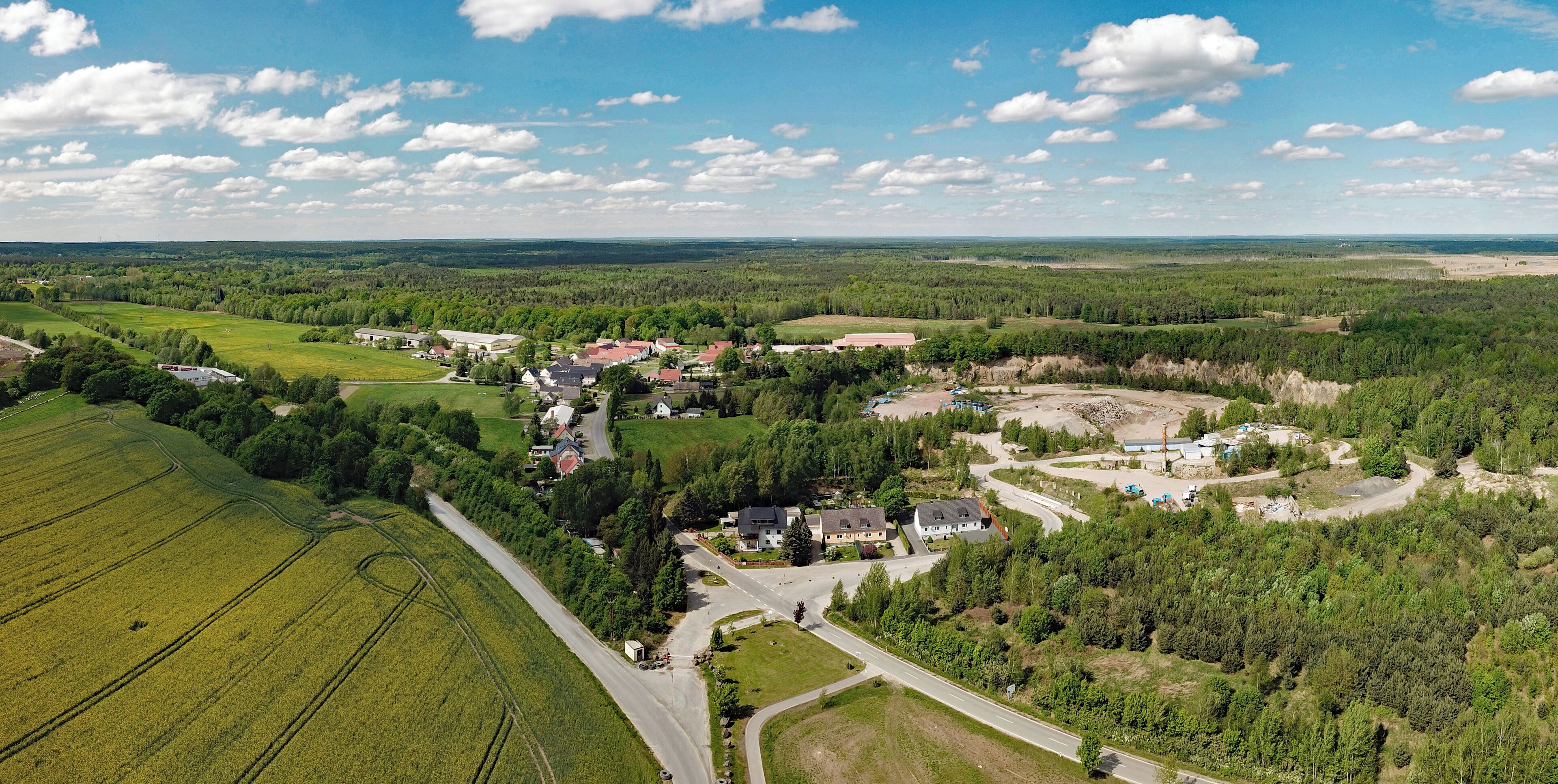 An aerial view of a rural area with fields, a small village, and a construction site.