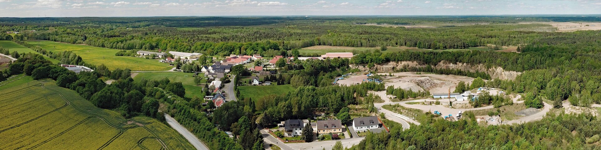 An aerial view of a rural area with fields, a small village, and a construction site.