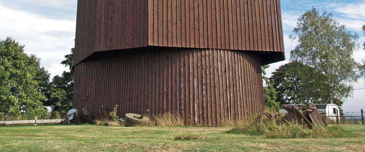 A large, wooden barn with a sloped roof, situated in a grassy field with trees in the background.