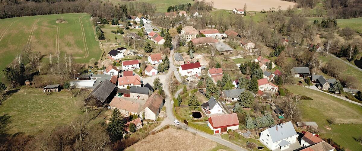 An aerial view of a rural village with houses, wind turbines, and rolling fields.