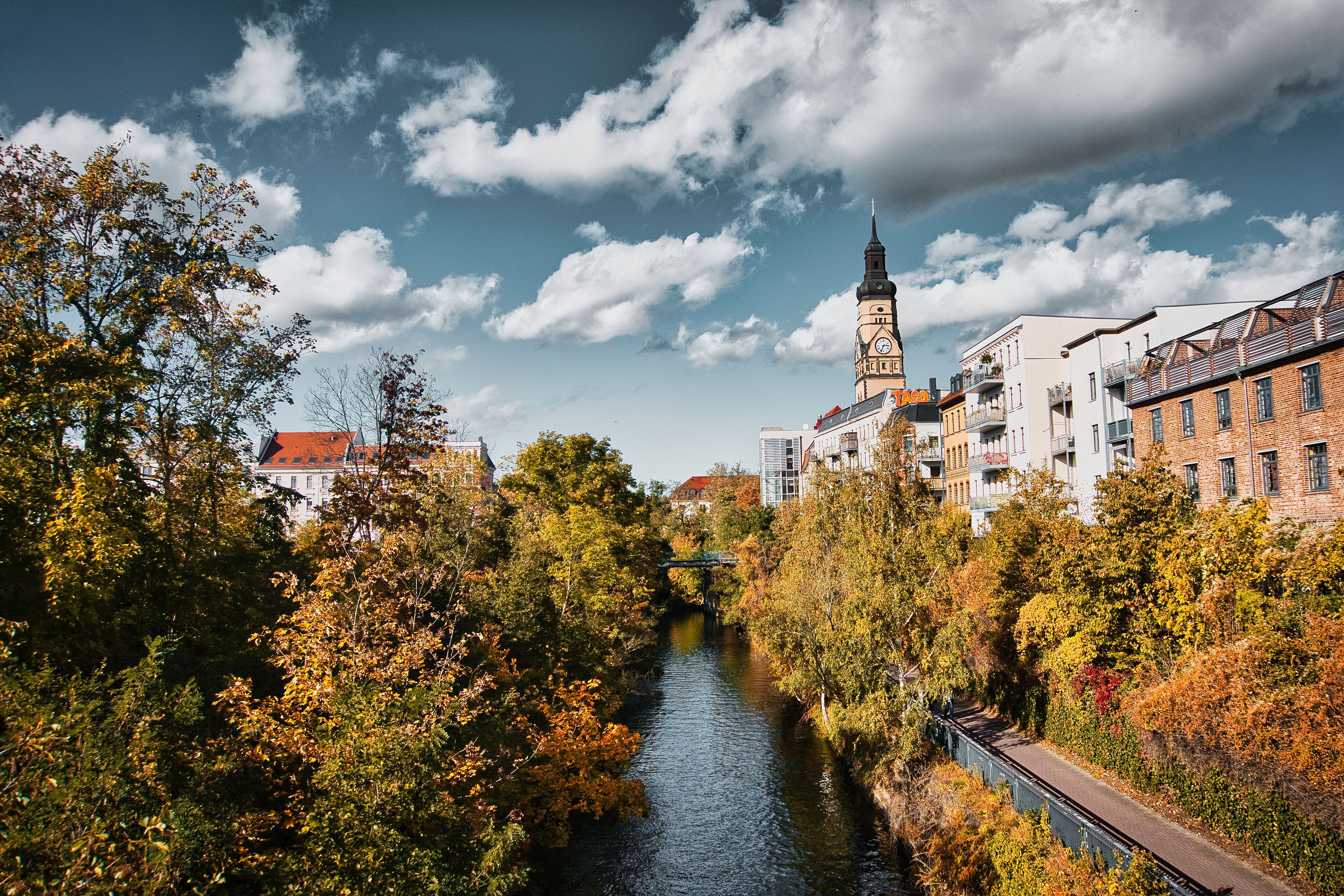 A river with a bridge, autumn trees, and historic buildings with a clock tower.
