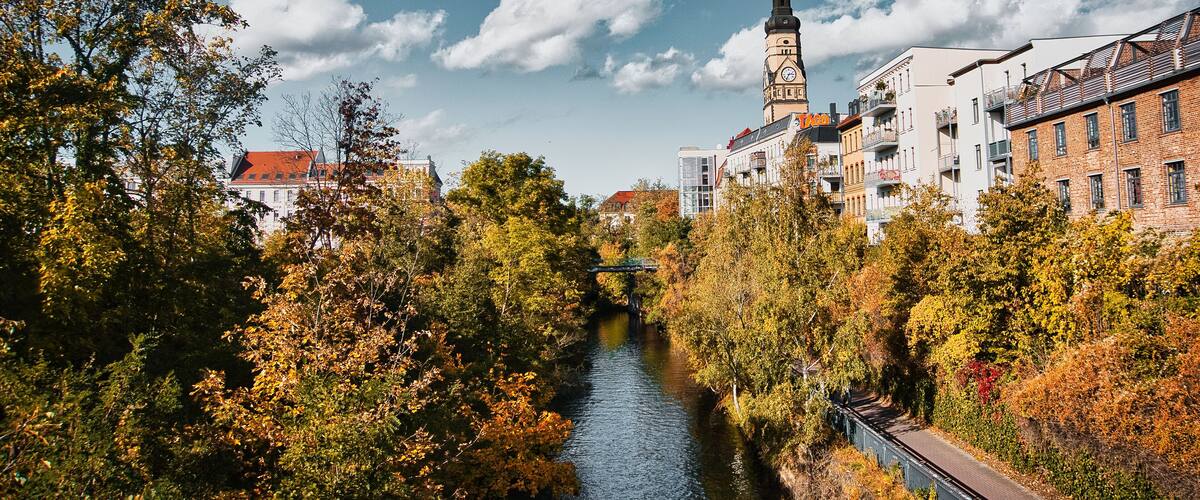 A river with a bridge, autumn trees, and historic buildings with a clock tower.