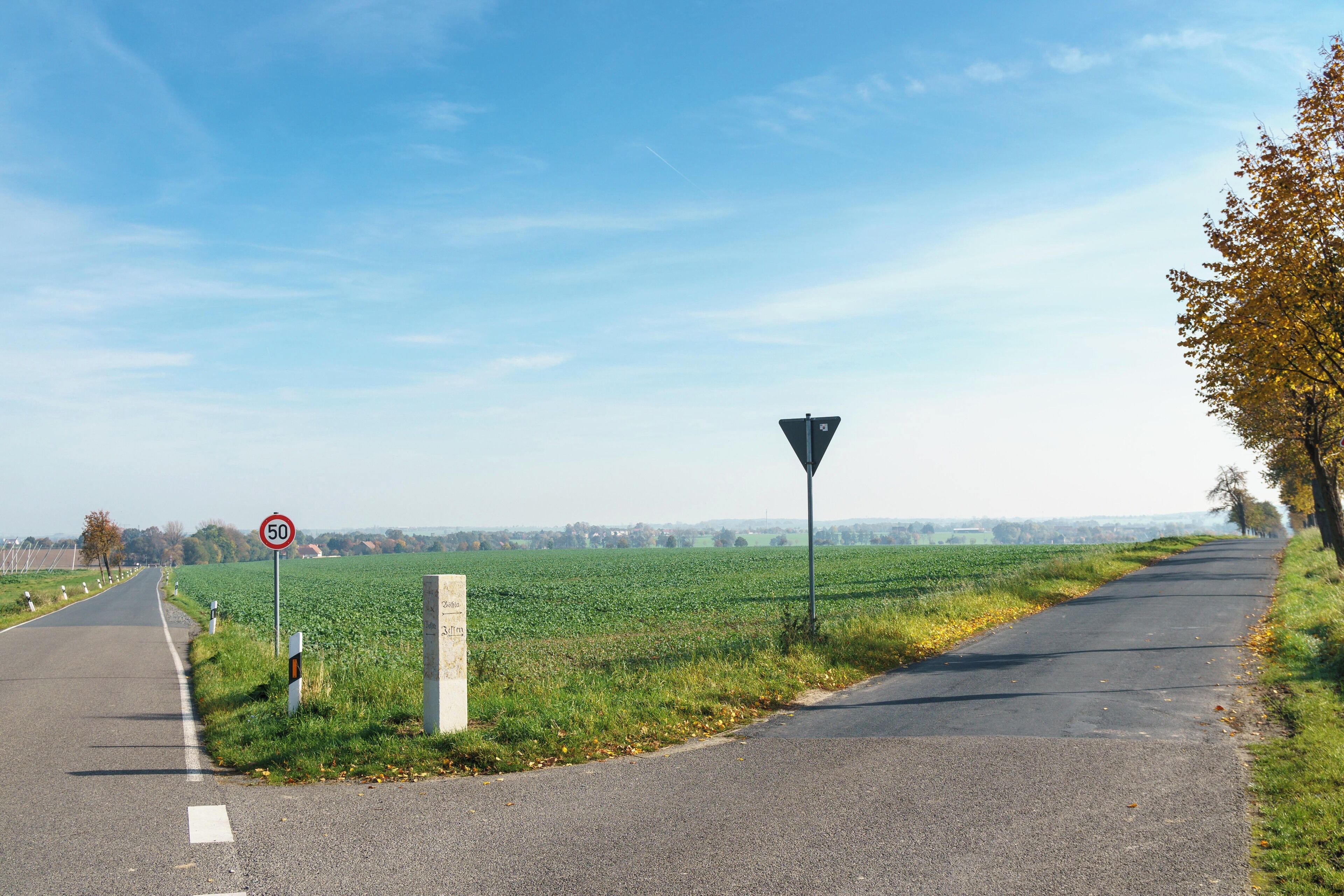 A rural road with a speed limit sign, a yield sign, and a field on one side.