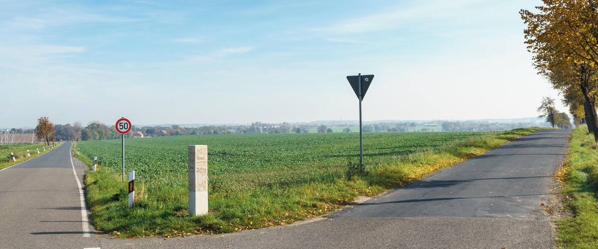 A rural road with a speed limit sign, a yield sign, and a field on one side.