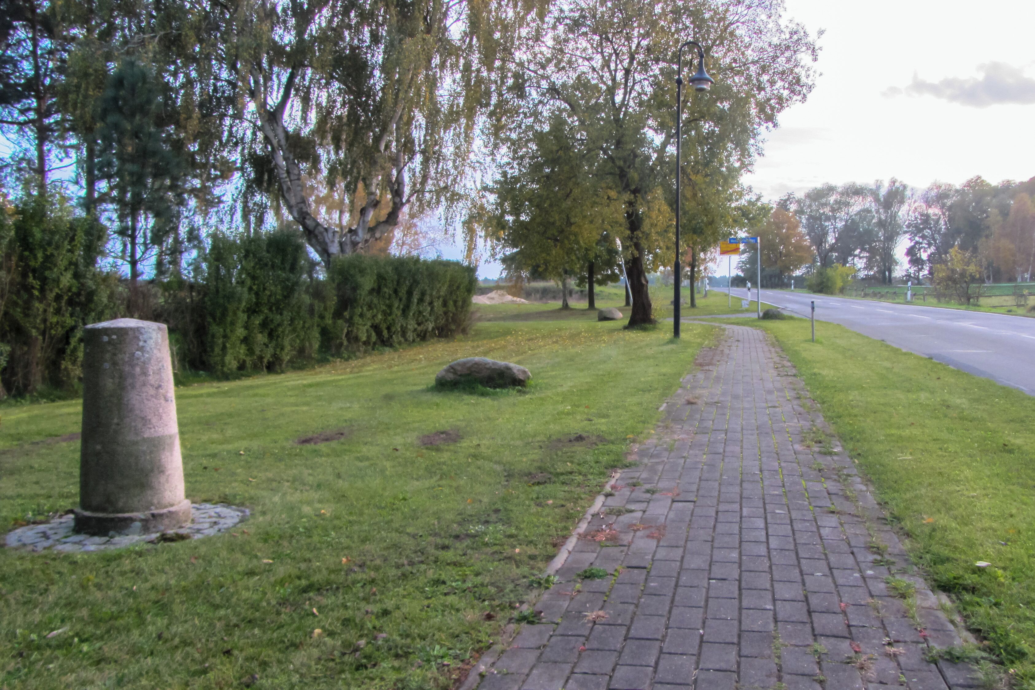 A paved pathway alongside a grassy area with trees and a stone monument.