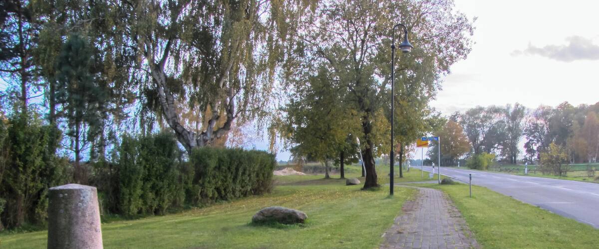 A paved pathway alongside a grassy area with trees and a stone monument.