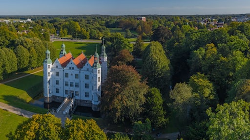 A large white castle with green roofs surrounded by lush greenery and a clear sky.