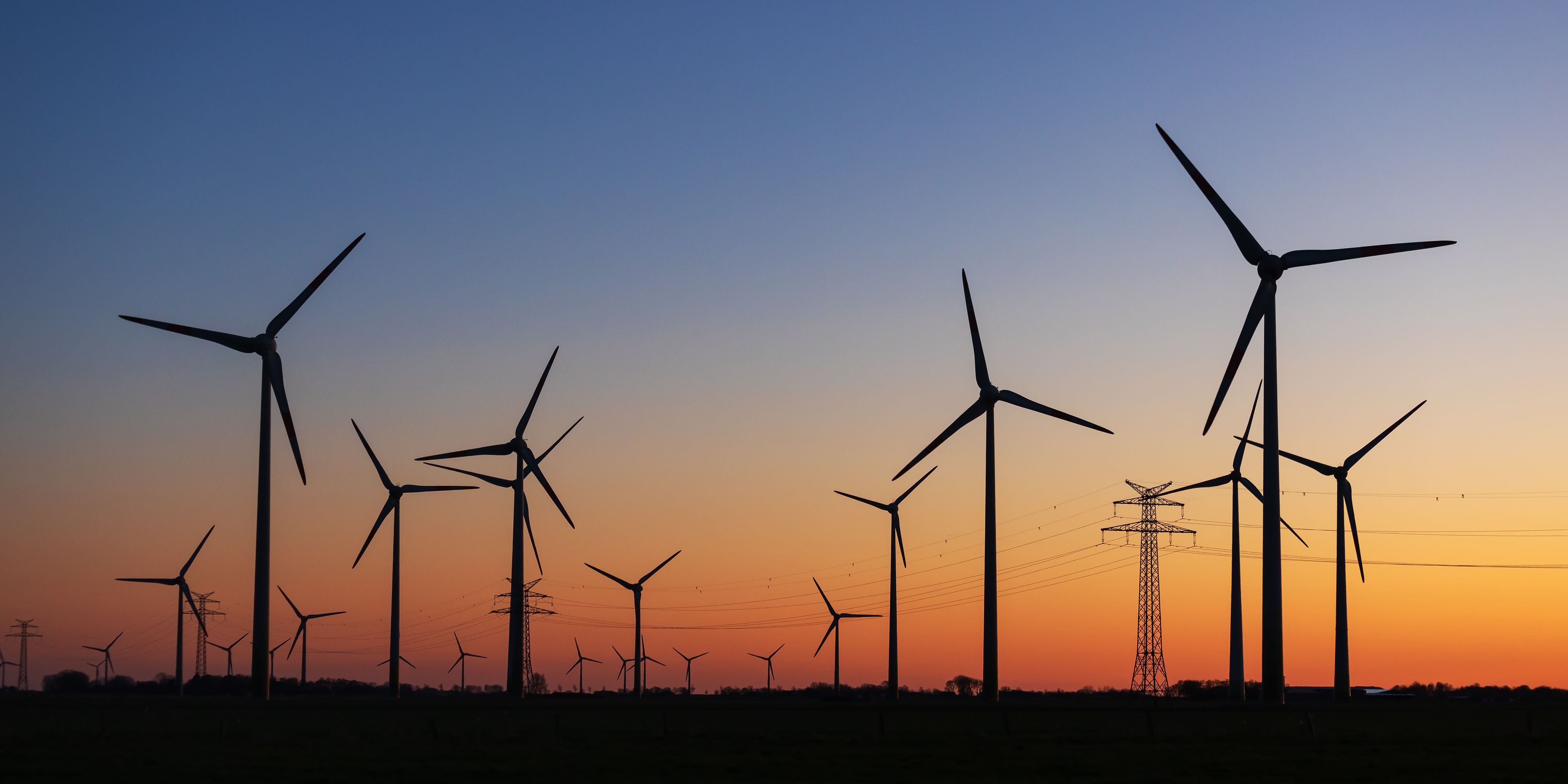 Eine Landschaft mit im Sonnenuntergangschatten stehenden Windkraftanlagen.