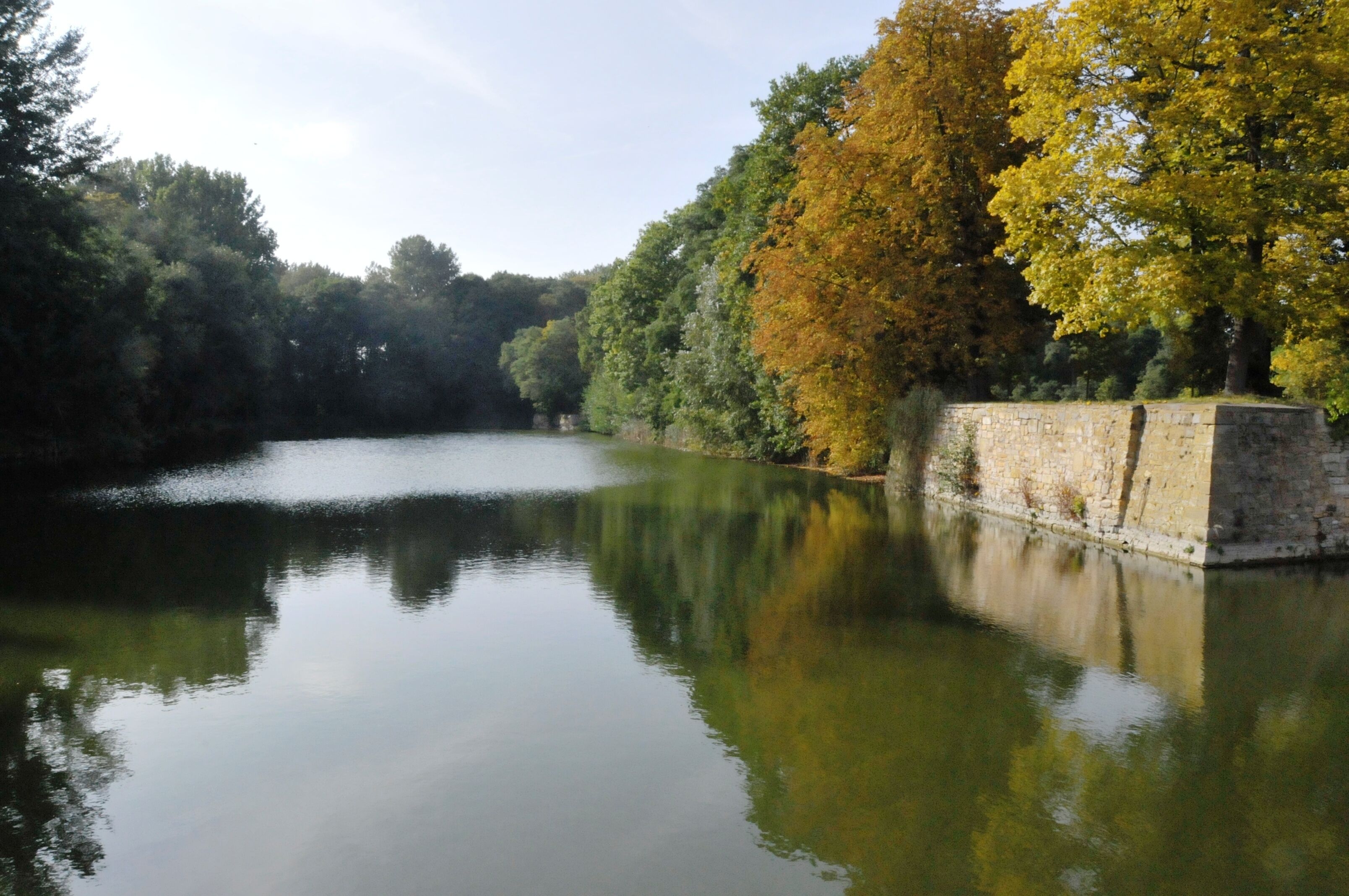 A calm river with autumn-colored trees reflecting on the water, surrounded by stone walls.