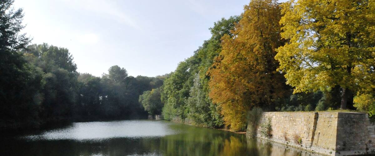 A calm river with autumn-colored trees reflecting on the water, surrounded by stone walls.