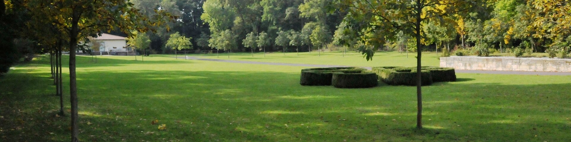 Un parque con césped verde, árboles y un muro de piedra.