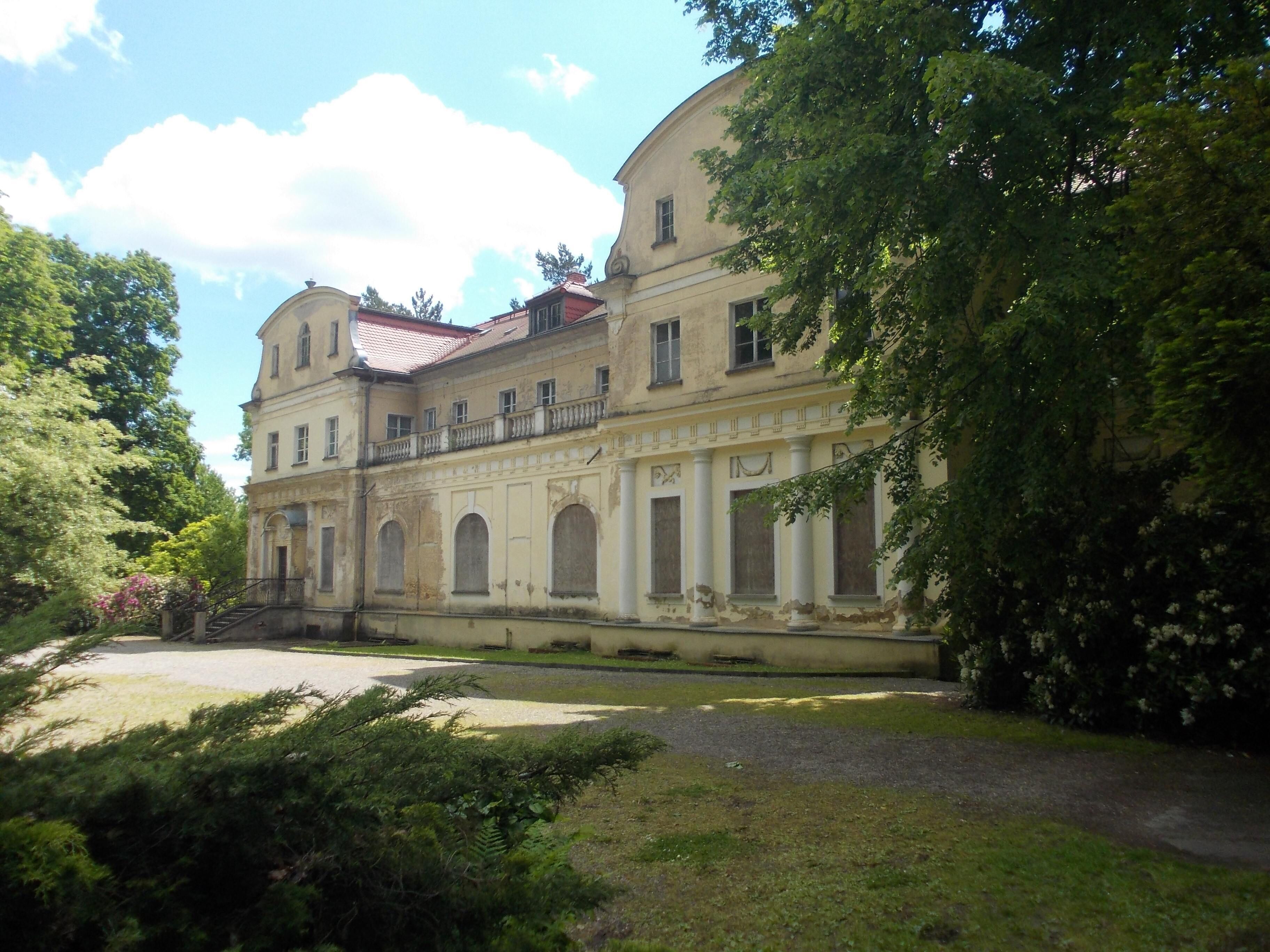 A historic building with classical architecture, surrounded by lush greenery and a well-maintained garden.