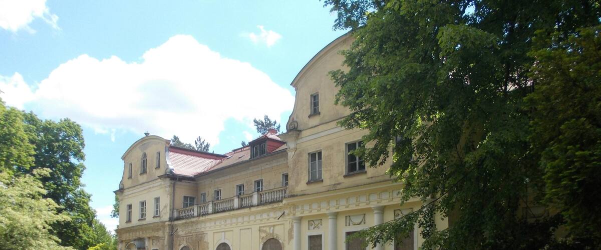 A historic building with classical architecture, surrounded by lush greenery and a well-maintained garden.