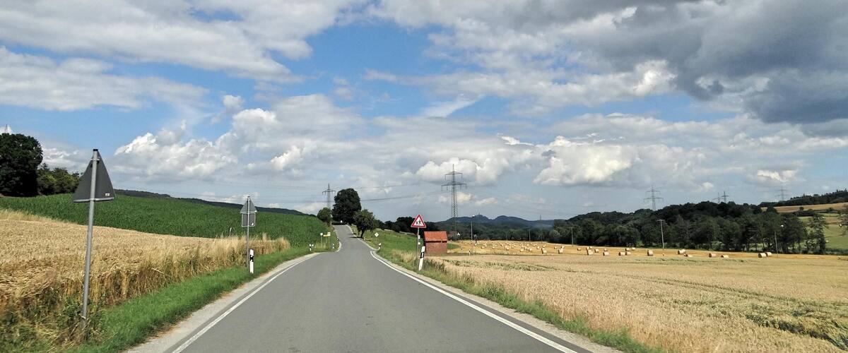 A rural road flanked by fields and a clear sky with clouds.