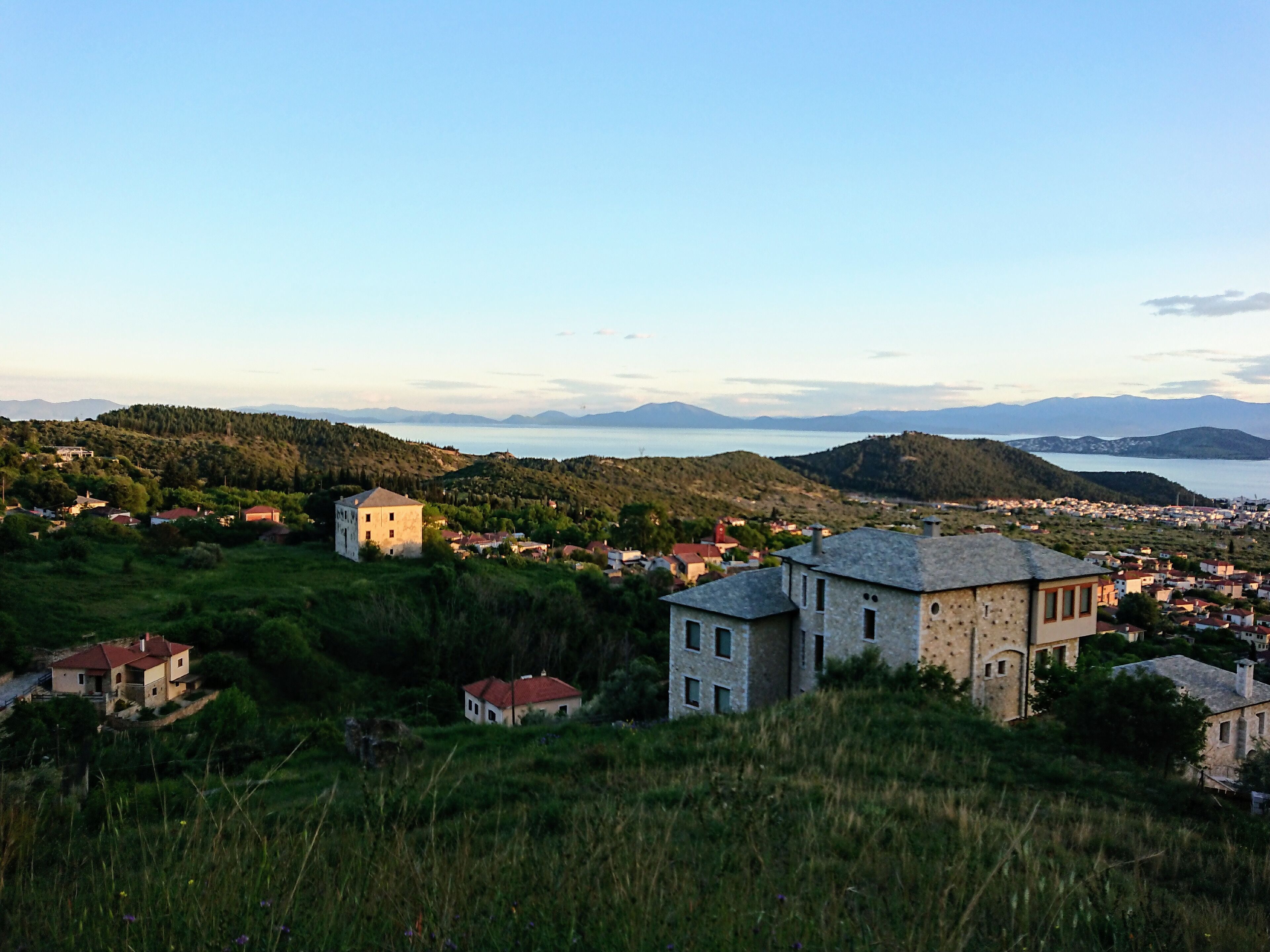 A coastal town with a prominent stone building in the foreground, surrounded by lush greenery and hills.