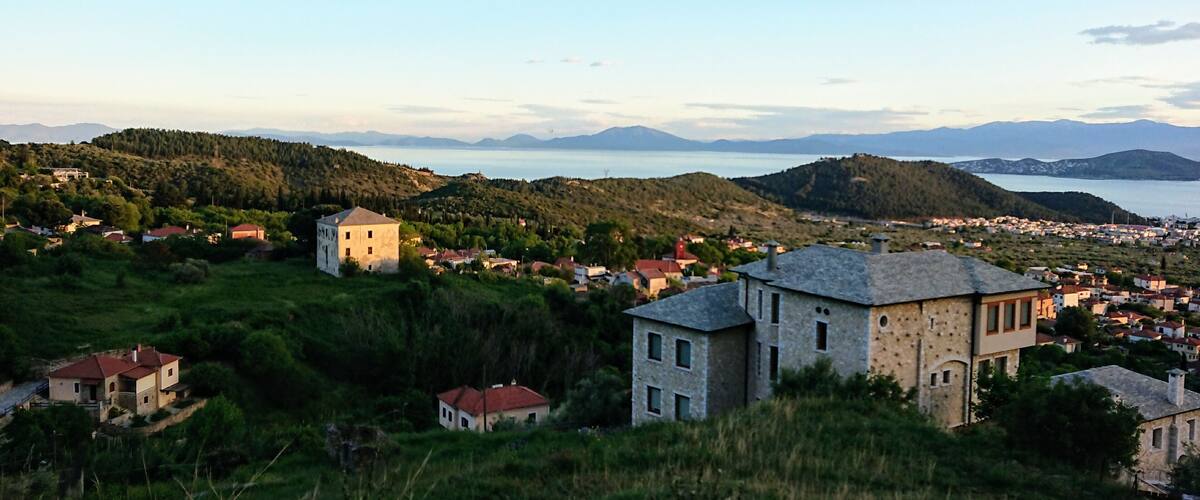 A coastal town with a prominent stone building in the foreground, surrounded by lush greenery and hills.