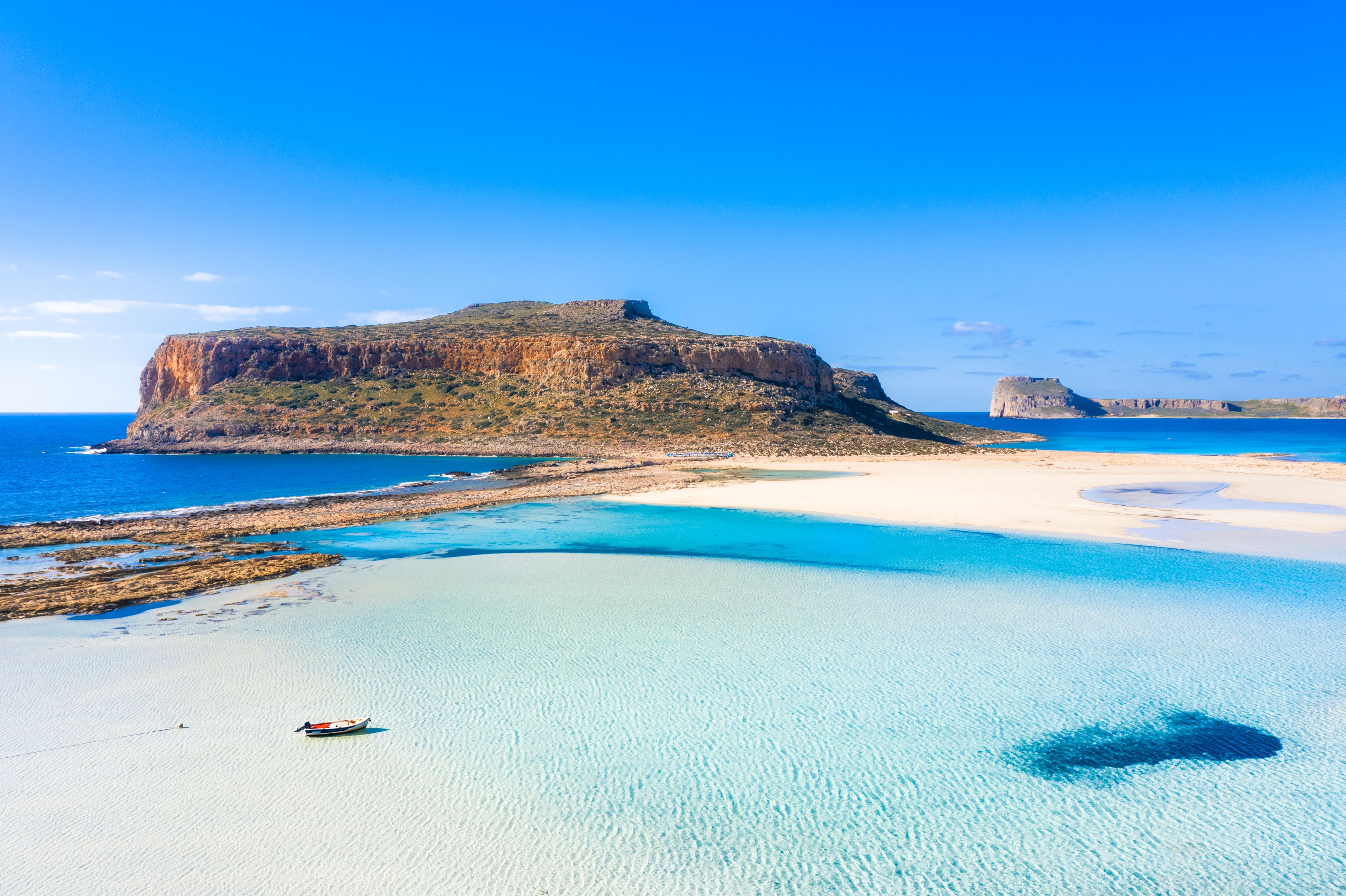 A coastal landscape with clear turquoise waters, a sandy beach, and a prominent rocky hill.