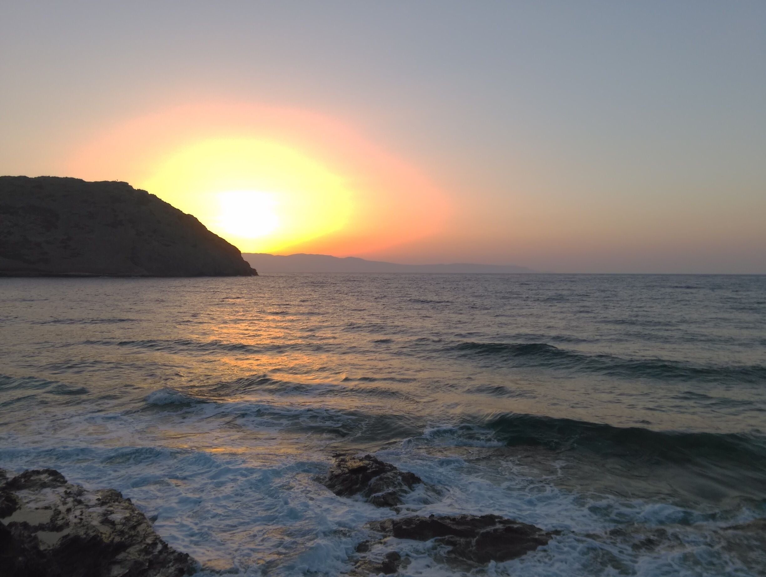 A sunset over the ocean with waves crashing onto rocks.