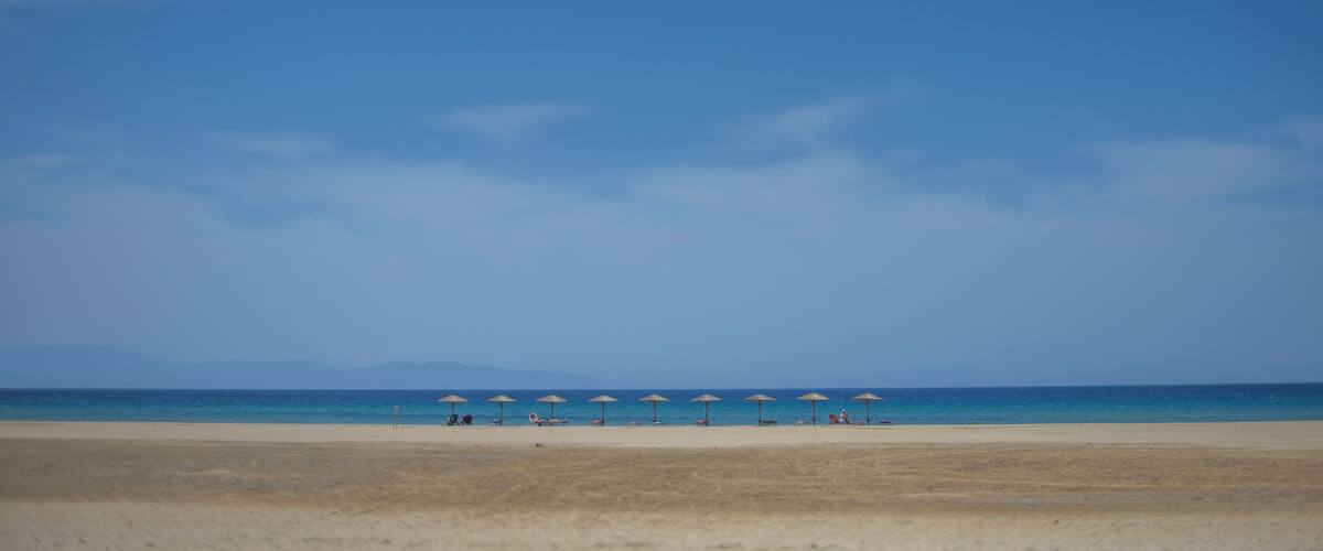 A beach with a clear sky, a sandy shore, and several umbrellas.