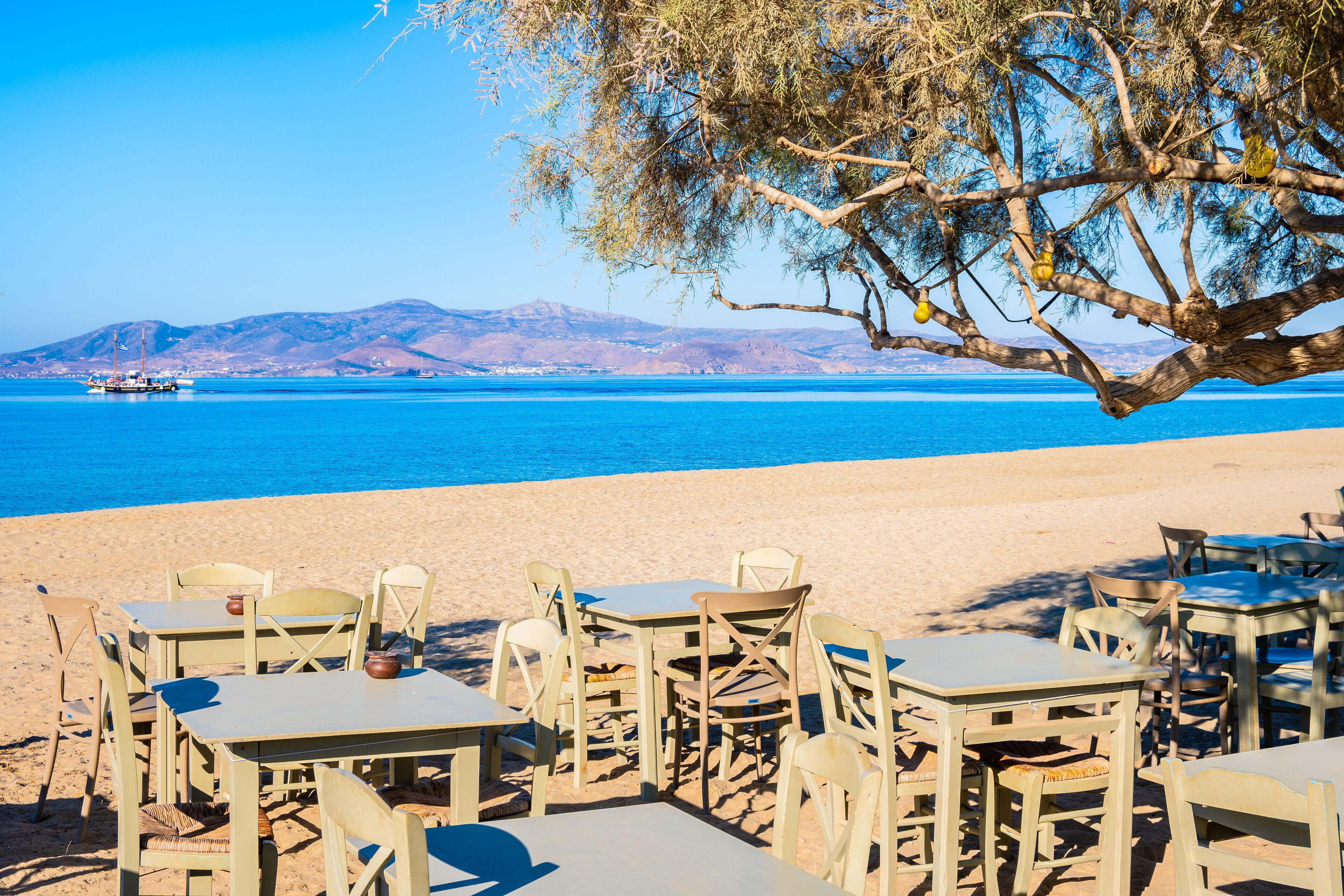 Tables with chairs in Greek taverna restaurant on Maragas beach and sea in distance, Naxos island, Cyclades, Greece
