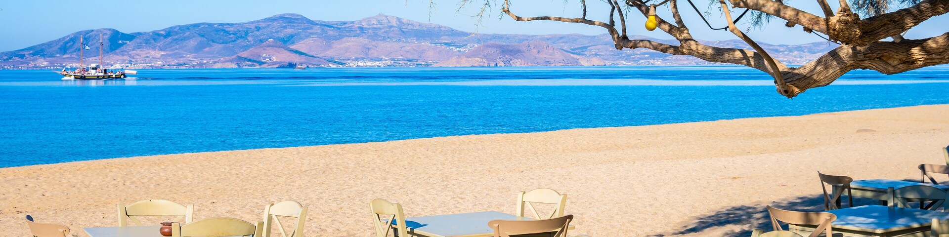 Tables with chairs in Greek taverna restaurant on Maragas beach and sea in distance, Naxos island, Cyclades, Greece
