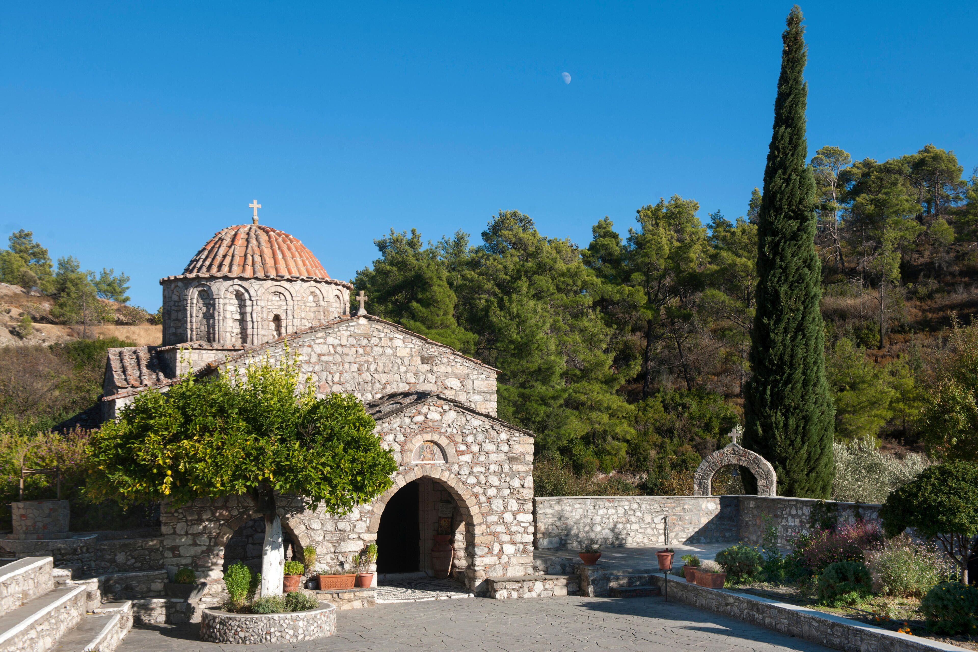 A stone church with a dome and cross, surrounded by trees and a clear sky.
