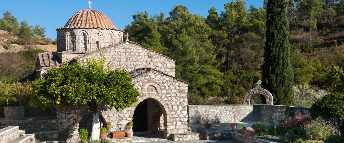 A stone church with a dome and cross, surrounded by trees and a clear sky.
