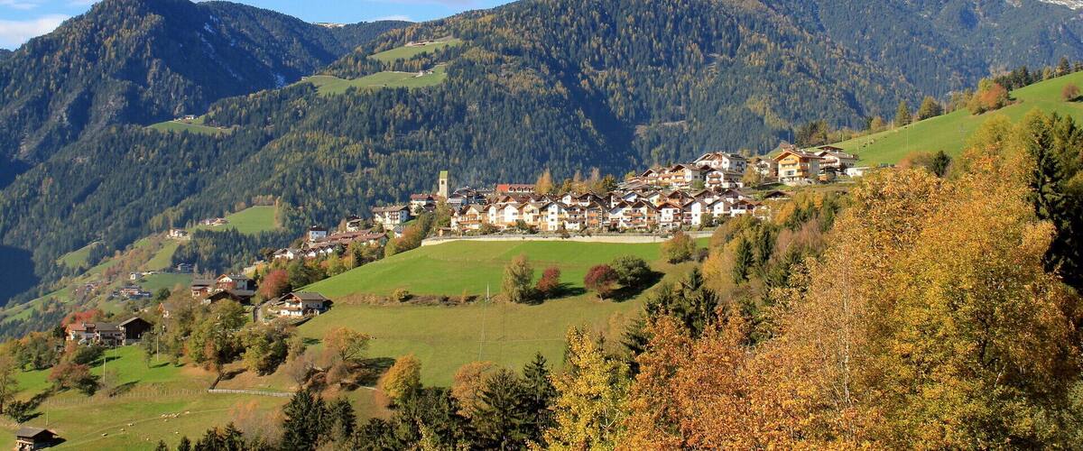 A mountain village with houses on a hillside, surrounded by forested mountains.