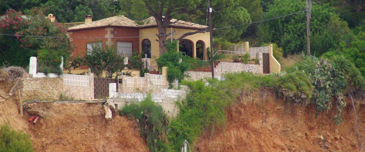 A hillside house with a stone retaining wall, surrounded by trees and vegetation.