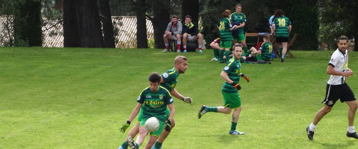 A grassy field with players in green and white uniforms, some sitting and others standing, likely during a sports event.