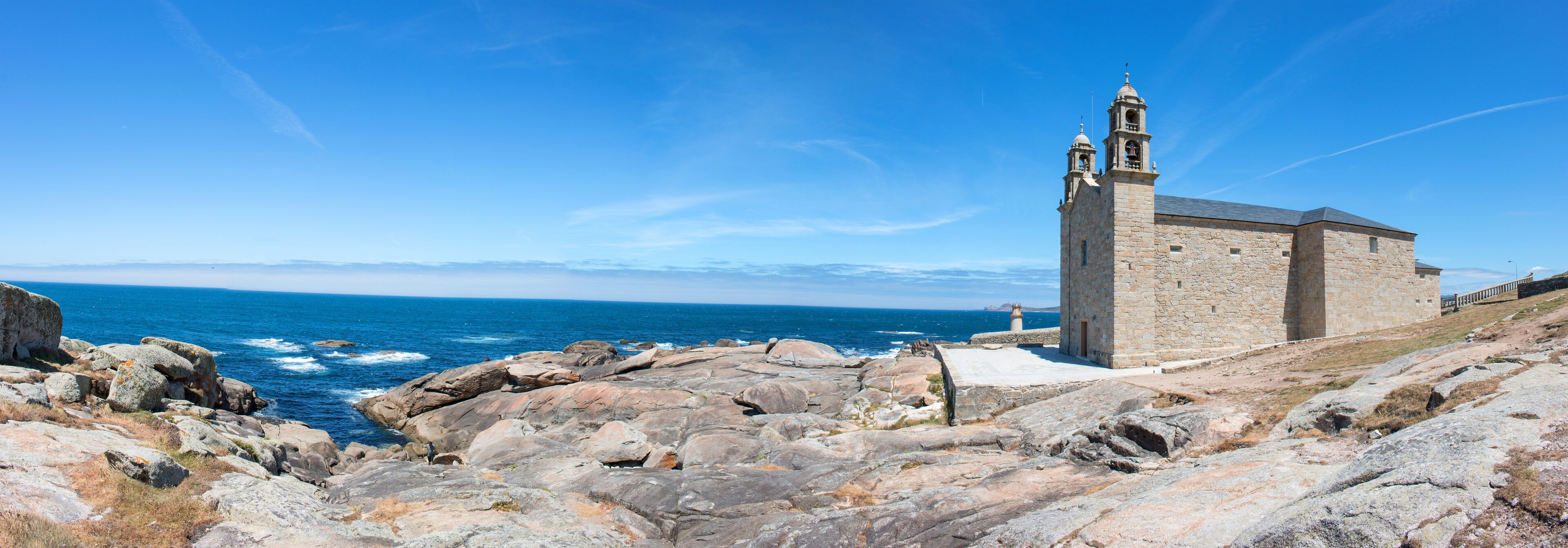 A coastal church with a bell tower, rocky shoreline, and the ocean in the background.