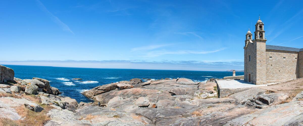 A coastal church with a bell tower, rocky shoreline, and the ocean in the background.