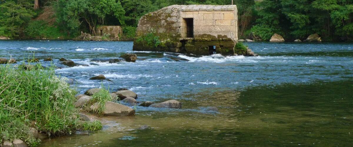 A stone structure on a riverbank surrounded by lush greenery.