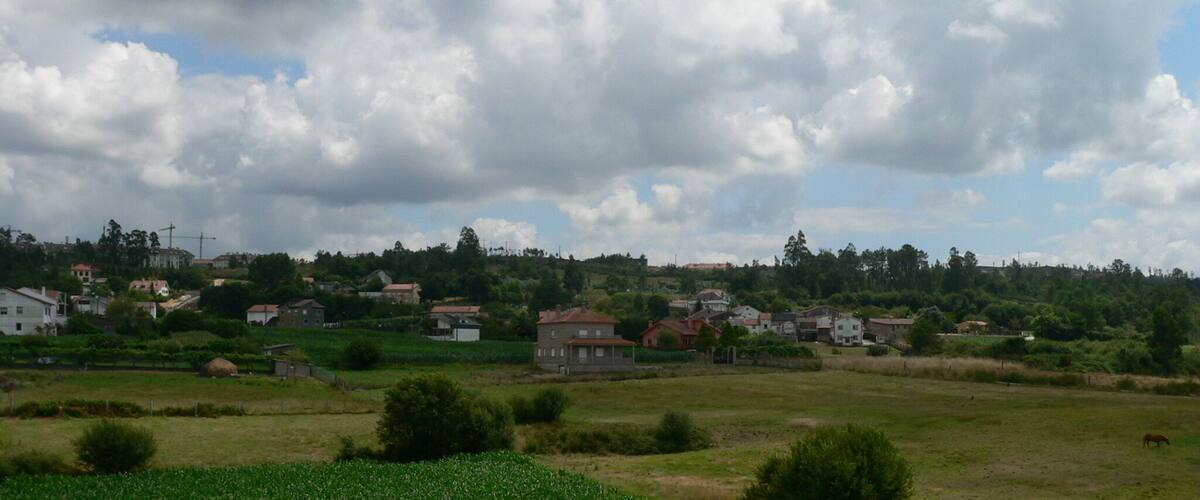 A rural landscape with houses, fields, and a cloudy sky.