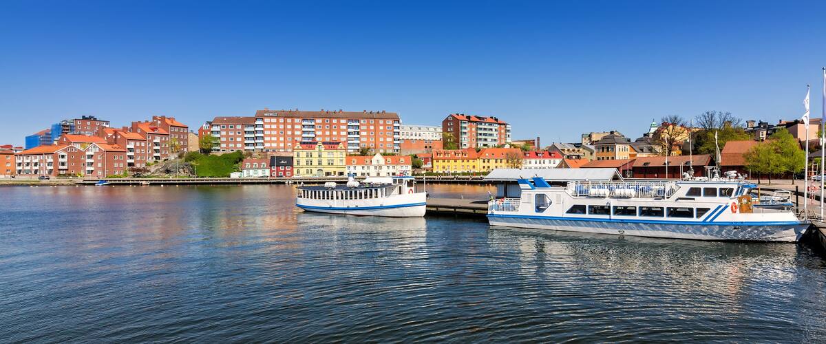 Two boats docked by a waterfront with colorful buildings in the background.