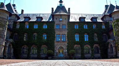 A historic building with a central clock tower, ivy-covered walls, and a symmetrical facade.