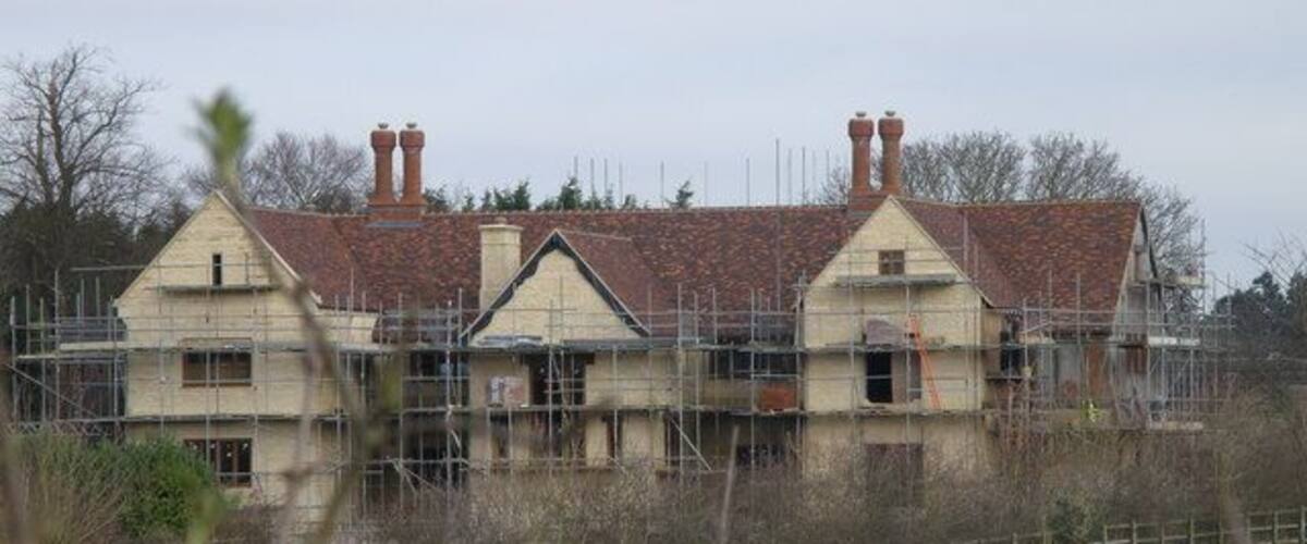 A two-story house with a red-tiled roof and a chimney, surrounded by scaffolding.