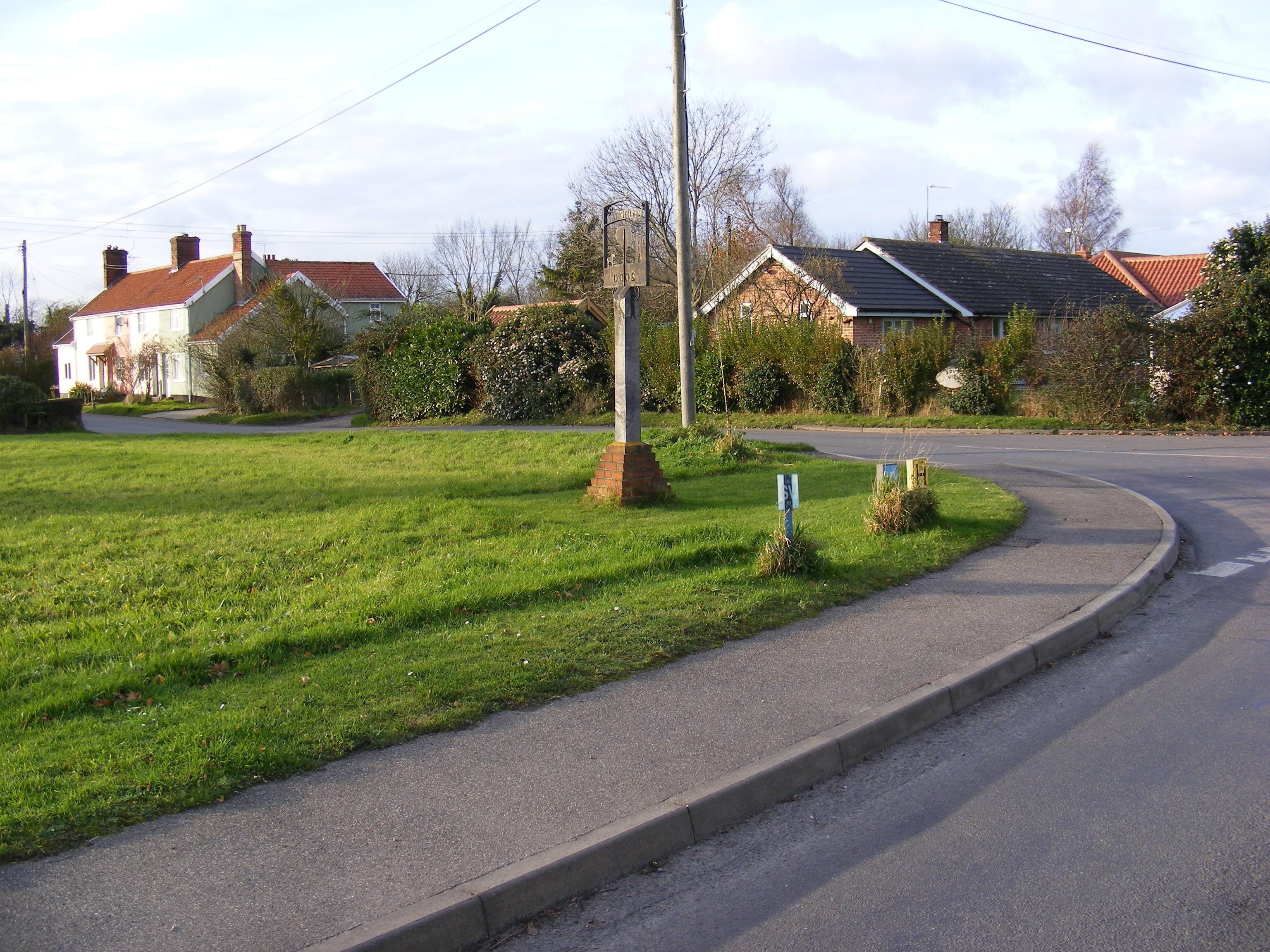 A residential street with houses, a grassy area, and a road curving to the right.